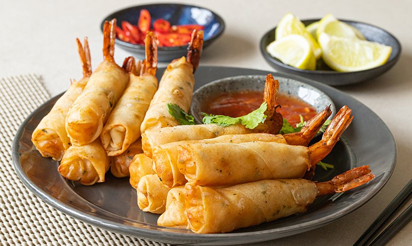 Crispy fried tail-on prawn rolls arranged on a white plate, showcasing their golden-brown exterior.