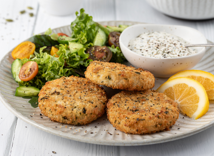 A plate of golden-brown fried fish cakes served with dipping sauce.