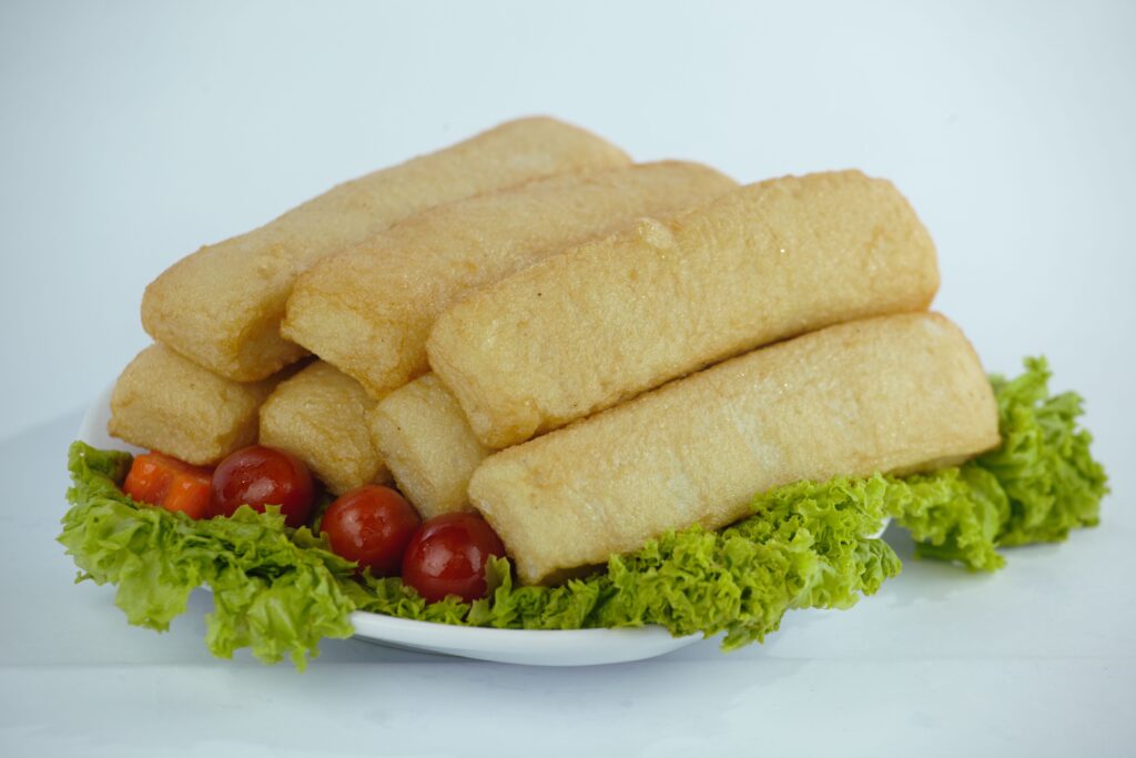Crispy fried fishcake sticks arranged neatly on a white plate, garnished with fresh herbs and lemon wedges.